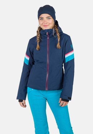 Navy blue ski jacket with pink and blue stripes on sleeves, zippered front, hood, and adjustable cuffs, paired with teal ski pants.