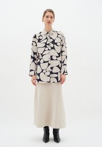 Prinditud pikkade varrukatega särk musta ja koorevärvi abstraktse mustriga, koos koorevärvi põrandapikkuse seeliku ja mustade pahkluu saapatega.