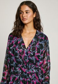 Blouse à motif floral en tissu transparent. Dotée d'un décolleté en V profond, de manches longues et d'une taille cintrée avec des nuances de rose, bleu et noir.