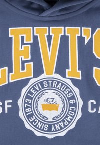 Felpa in cotone blu con un grande logo "LEVI'S" bianco e giallo, con un emblema che mostra un orso e un rettangolo giallo sottostante.