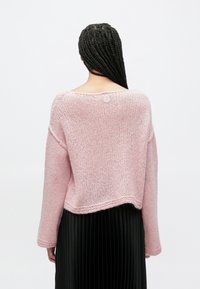 Ροζ πλεκτό πουλόβερ με άνετη εφαρμογή, φαρδύ λαιμόκομμα και ριμπ μανσέτες. Διαθέτει στρογγυλή λεπτομέρεια με κουμπί στο πίσω μέρος και cropped μήκος.