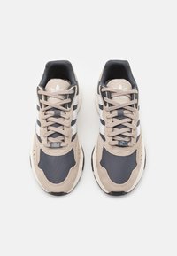 Sneakers beige e navy realizzati in materiali sintetici in rete e suede, con strisce bianche e dettagli grigi, punta rotonda e chiusura con lacci.