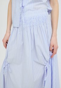 Jupe à rayures bleu clair et blanc avec une taille smockée et des sections froncées nouées avec des nœuds de chaque côté, portée avec un haut assorti.