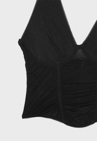 Top noir cintré sans manches avec col en V, tissu en mesh et bordure festonnée le long des bords sur un fond clair uni.