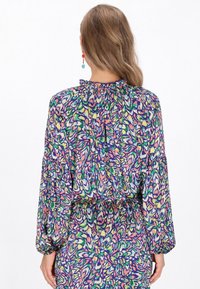 Színes blúz selymes anyagból, rózsaszín, zöld és kék árnyalatú virágmintával. Lebegő ujjak és fodros nyakrész részlet.