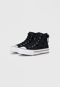 Fekete magas szárú sneaker, pöttyös textúrával, fehér gumitalppal és toe cap-pel, fűzős kialakítással és hátsó húzóval a könnyű felvétel érdekében.