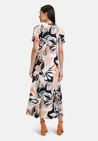 Maximeikka, jossa on musta, valkoinen ja persikkainen kukkakuvio, lyhyet hihat ja hulmuava siluetti. Yhdistetty oransseihin palkeellisiin sandaaleihin.