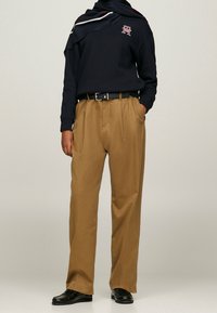 Sudadera marina con logotipo, pantalones de tiro alto marrones, cinturón negro y zapatos negros. Textura suave, corte relajado, diseño casual.