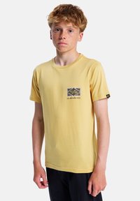 Žluté bavlněné tričko s krátkými rukávy, s logem na přední kapse. Hladká textura, klasický kulatý výstřih, uvolněný střih.