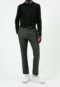 Svart texturerad tröja, grå mönstrade byxor med bälte, och vita sneakers. Skjortan har en liten krage.