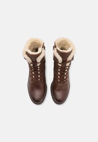 Botas de cuero marrón con forro de borreguito, parte delantera con cordones y detalle de cremallera. Superficie texturizada y suela de goma resistente para un buen agarre.