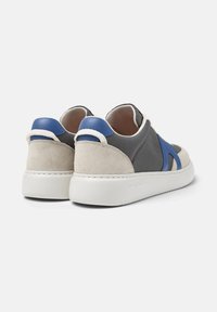 Gray and beige sneaker with blue accents, featuring a mix of suede and fabric, textured upper, and a white rubber sole.
