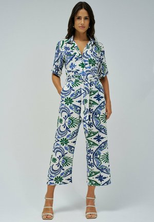 Un mono multicolor en blanco, con patrones florales en azul y verde, mangas cortas, un cuello con solapa y una cintura ceñida con cinturón.