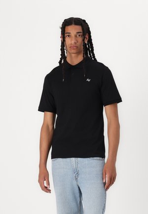Polo noir à manches courtes, col côtelé et petit logo blanc sur la poitrine, associé à un jean en denim bleu clair.