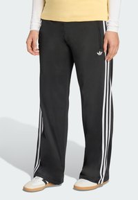 Black athletic pants featuring three white side stripes and a small logo on the hip. Made of smooth fabric with a relaxed fit.