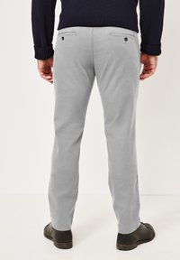 Light gray chinos with flat pockets and button accents, complemented by a dark sweater and black shoes. Smooth texture and straight-leg design.