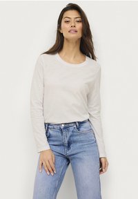 Long-sleeve, light beige crew neck t-shirt made of soft fabric. Paired with mid-rise blue denim jeans featuring subtle wash details.
