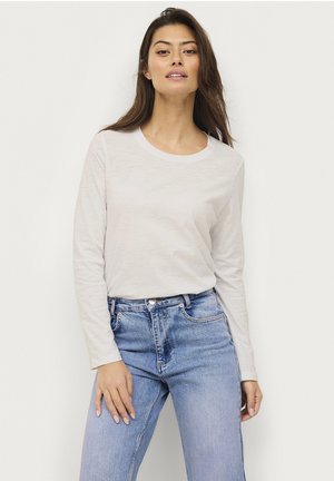 Long-sleeve, light beige crew neck t-shirt made of soft fabric. Paired with mid-rise blue denim jeans featuring subtle wash details.
