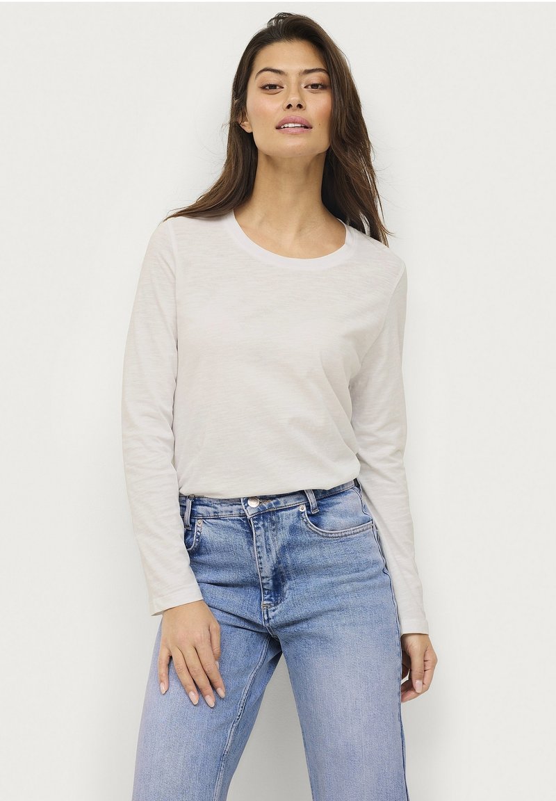 Long-sleeve, light beige crew neck t-shirt made of soft fabric. Paired with mid-rise blue denim jeans featuring subtle wash details.