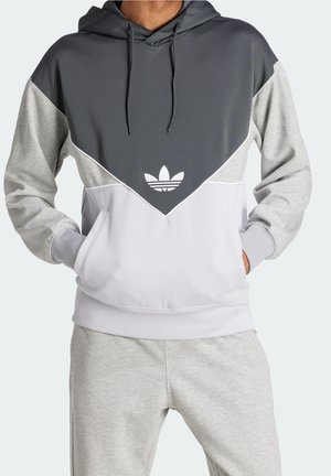 Mann trägt einen Hoodie mit dunkelgrauen, hellgrauen und weißen Farbblöcken sowie weißem Adidas-Trefoil-Logo, kombiniert mit hellgrauen Jogginghosen.