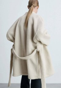 Burgundska fleece jakna s teksturiranom površinom, oversized kroja, širokim rukavima i vezanom remenom u struku. Pogled straga bez vidljivih kopčanja.