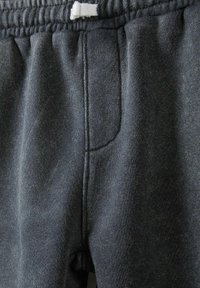 Mörkgrå sweatpants tillverkade av mjukt, strukturerat tyg. Har elastisk midja med snodd och en sidficka. Enkel, avslappnad design.