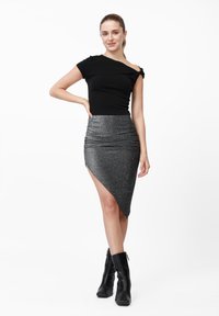 Μαύρο τοπ με έναν ώμο σε συνδυασμό με ασημένια φούστα ψηλόμεση με ασύμμετρο τελείωμα, διακοσμημένη με υφή και λαμψεις. Το μοντέλο φοράει μαύρα μποτάκια αστραγάλου.