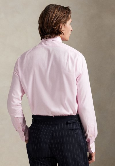 Šviesiai rožinė marškiniai su mygtukais ir nugaros yoke, derinami su tamsiai mėlynomis dryžuotomis kelnėmis, kuriose yra nugaros kišenės ir šoninės reguliavimo detalės.