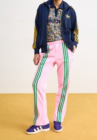 Adidas träningsoverall med en marinblå jacka med gula ränder, blommig pikétröja, rosa byxor med gröna ränder och lila sneakers.