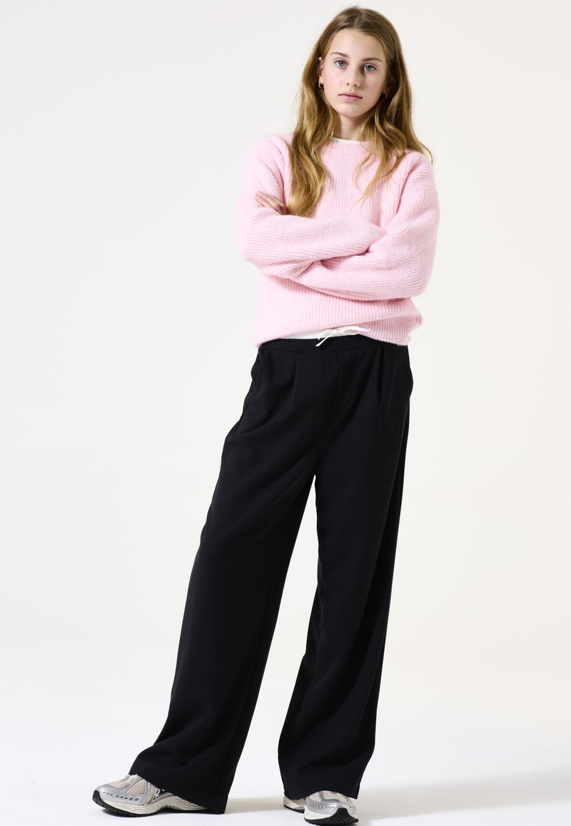 Rosa geripptes Strickoberteil, schwarze weite Hosen mit elastischem Bund und silberne Sneaker. Schlichte, lässige Passform mit einer entspannten Silhouette.