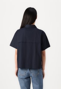 Camisa de manga corta azul marino con cuello de punta, que presenta un detalle de yugo en la parte posterior, combinada con unos vaqueros de denim azul de talle alto.