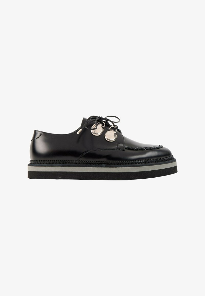 Chaussure noire en cuir à lacets avec semelle épaisse et œillets ronds métalliques, vue de profil sur fond blanc.