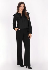 Sort outfit bestående af en cropped top med flæser på skuldrene og en bindebånd ved halsen, parret med højtaljede, vidde bukser. Glat stofstruktur.