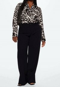 Blusa a maniche lunghe a righe bianche e nere con colletto, abbinata a pantaloni neri a vita alta e gamba larga, realizzati in tessuto liscio.