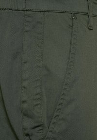 Olive green fabric with a smooth texture, featuring stitched seams and a side pocket detail. The design includes a fitted waistband.