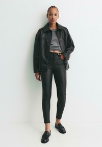Crna kožna overshirt jakna, sivi skraćeni top, crne tajice viskog struka, crni loafersi. Karakteristike uključuju dugmad sprijeda i elegantan kroj.