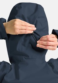 Marineblauer wasserdichter Jacke mit verstellbarem Kapuze. Verfügt über einen Kordelzug und einen Stopper für eine optimale Passform. Das Material wirkt glatt und leicht.