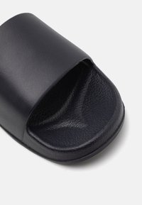 Schwarze Rutschsandale mit einer glatten oberen Oberfläche und einer strukturierten Innensohle. Minimalistisches Design mit einem breiten Riemen und abgerundeten Kanten. Strapazierfähiges Materialfinish.