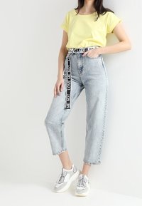 T-shirt giallo a maniche corte, jeans azzurri a vita alta con una cintura nera etichettata "LOVE ME NOT", e sneakers bianche con accenti grigi.