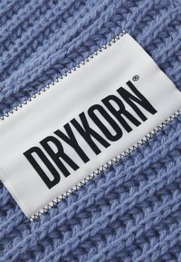 Tessuto lavorato a maglia blu con un motivo testurizzato, dotato di un'etichetta bianca con "DRYKORN" in grassetto nero e cuciture decorative.