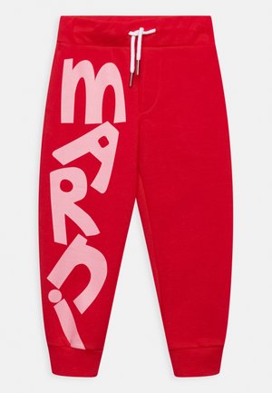 Pantalon de survêtement rouge en coton, avec un grand texte graphique rose le long de la jambe gauche, taille élastique avec cordon de serrage, et bas resserrés.