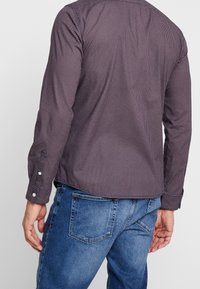 Camicia a maniche lunghe a quadri in viola scuro con pois bianchi, con polsini con bottoni e taglio dritto. Abbinata a jeans in denim blu.