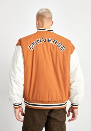 Chaqueta bomber naranja y blanca con rayas horizontales en los puños y la cintura, con "CONVERSE" bordado en la parte posterior.