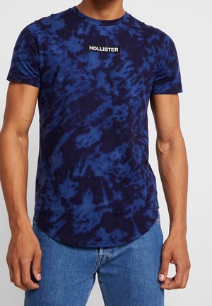 T-shirt a manica corta e colletto tondo in tie-dye blu navy, con il logo "HOLLISTER" in bianco e nero sul petto. Materiale in cotone.