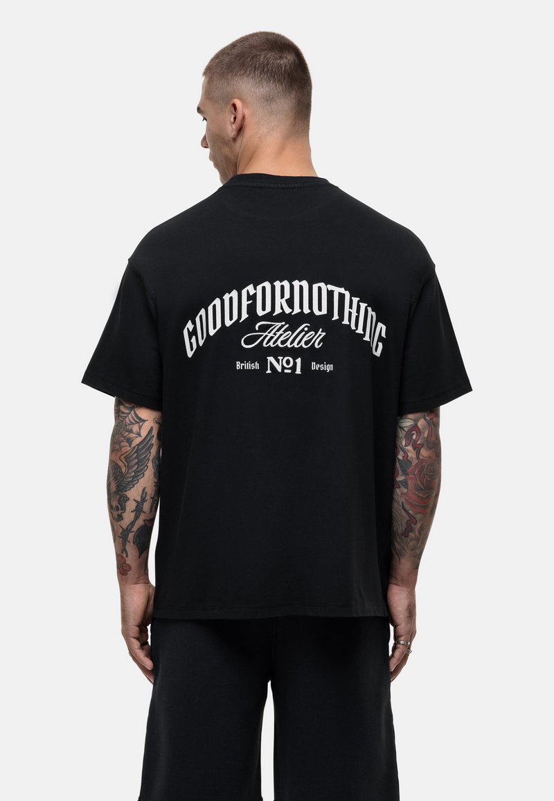Zwarte katoenen T-shirt met gedurfde witte tekst op de achterkant: "GOODFORNOTHING Atelier British No1 Design." Ontspannen pasvorm, korte mouwen.