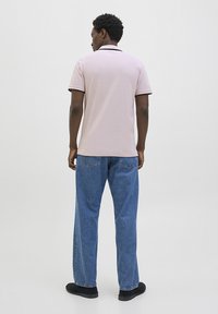 Polo skjorte i lys pink med en sort krave, parret med løse blå jeans og sorte sko, set fra ryggen. Simpelt teksturmønster.