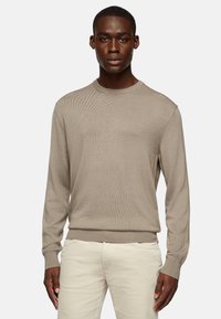 Light beige long-sleeve sweater with a textured knit design, crew neck, and ribbed hem. Worn with light-colored pants.