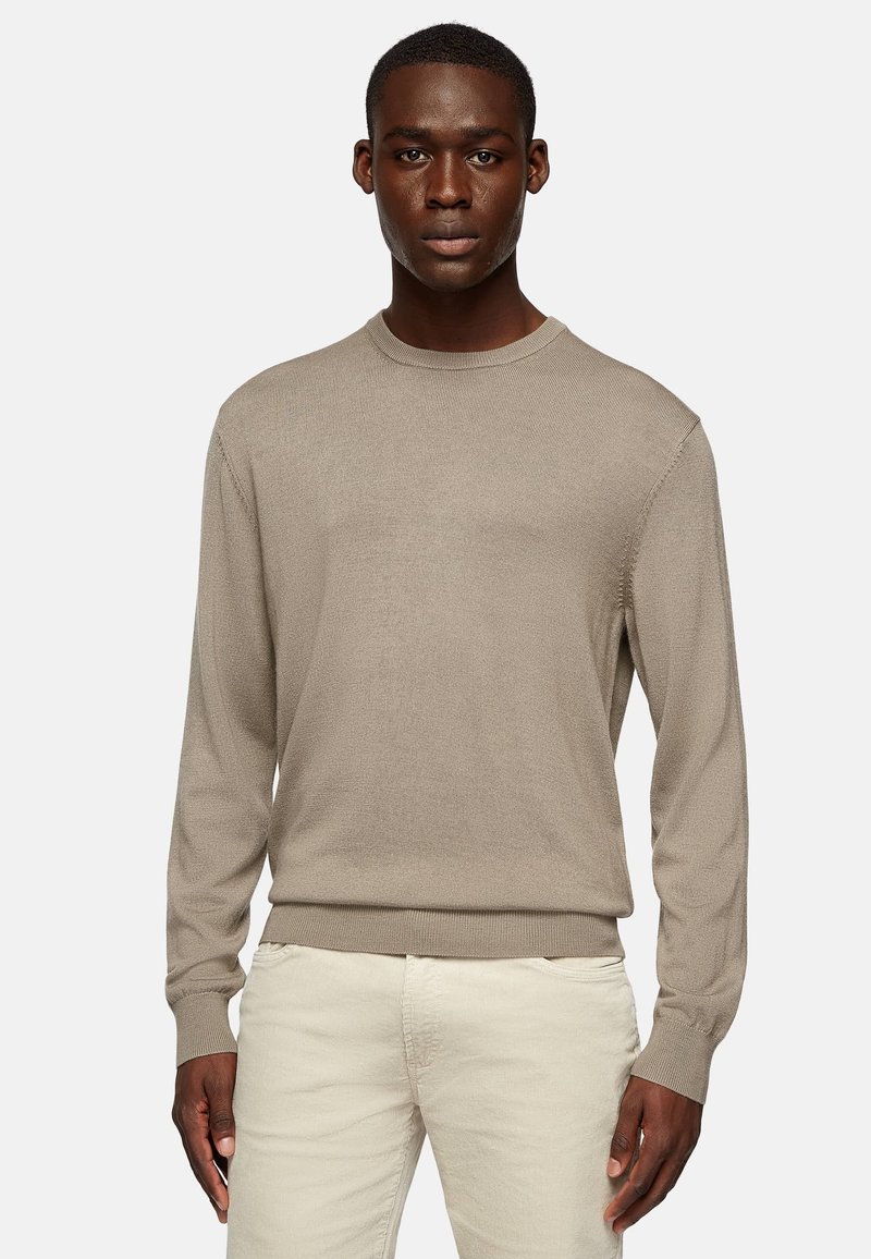Light beige long-sleeve sweater with a textured knit design, crew neck, and ribbed hem. Worn with light-colored pants.