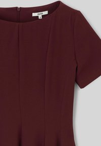 Robe bordeaux à manches courtes, col rond, tissu texturé et détails plissés. Dispose d'une fermeture éclair dissimulée au dos.