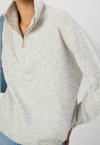 Light gray knit sweater with a high collar and half zip. Textured fabric with a subtle pattern, featuring rose gold hardware accents.
